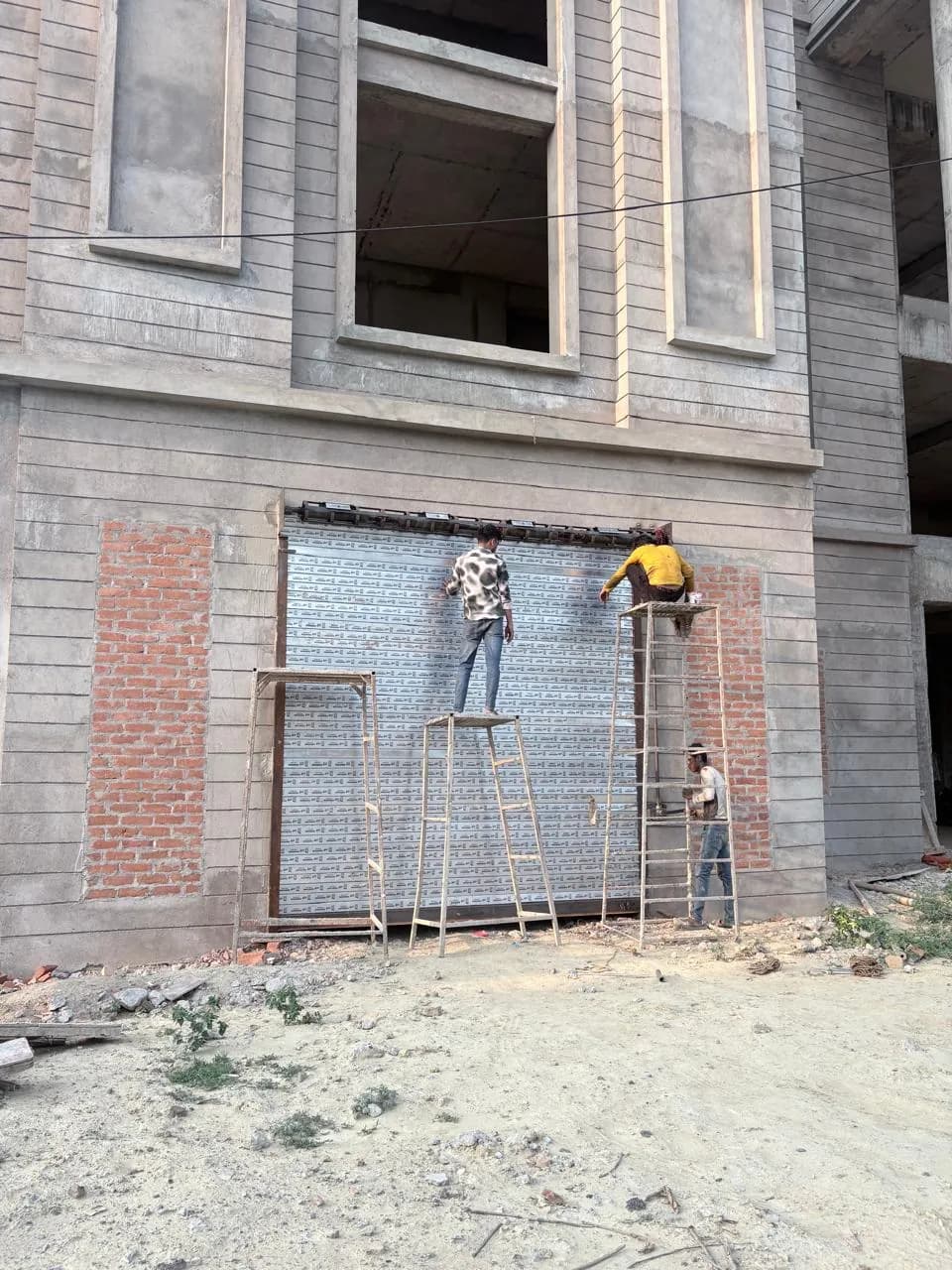 Workers fixing façade panels between brick piers