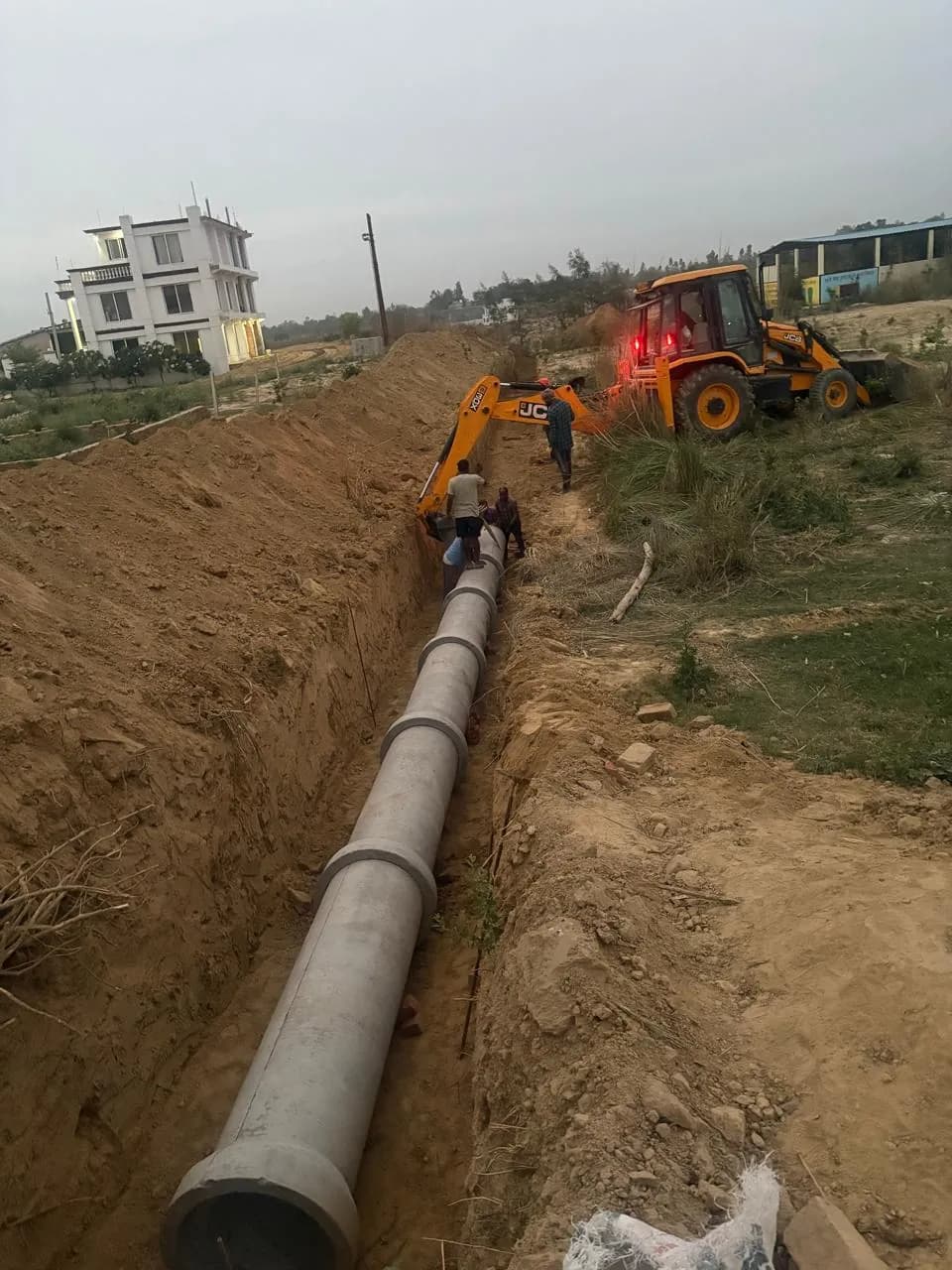 Concrete pipe laid in a trench with an excavator beyond