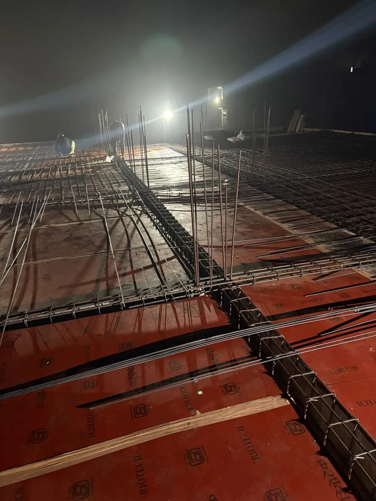 Slab reinforcement over red shuttering under site lights at night