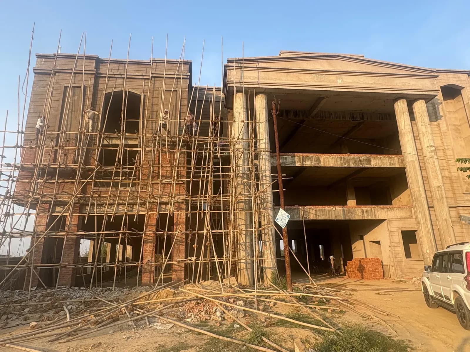 Classical façade with tall columns and pediment under bamboo scaffolding in warm evening light