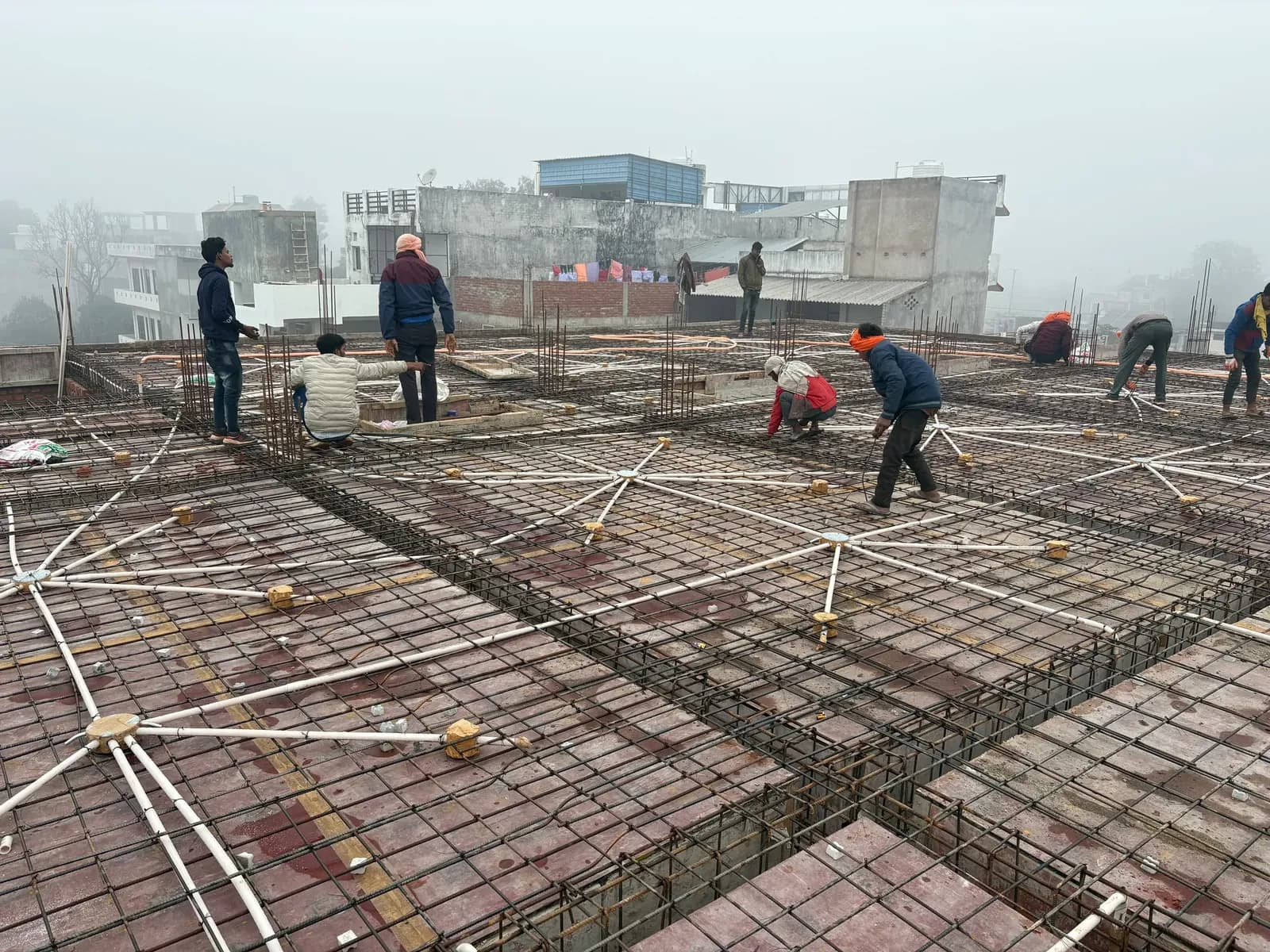 Workers setting slab reinforcement with conduits on a large roof